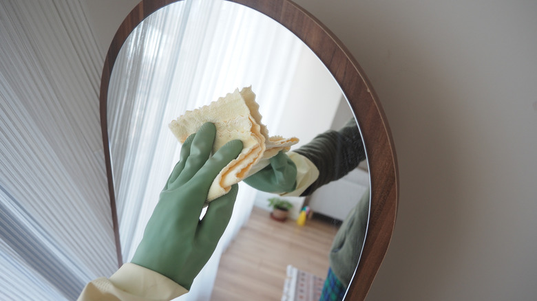 Gloved hand wiping down mirror with cloth.