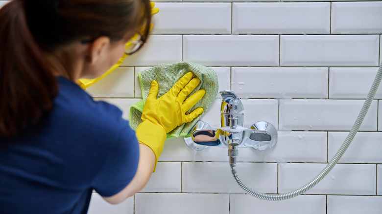 Woman wiping down bathroom tile with cloth.