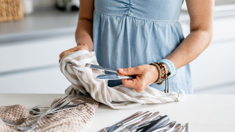 Woman wiping silverware with cloth.