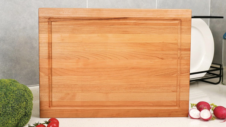 A cherry wood cutting board standing on its side on a kitchen counter