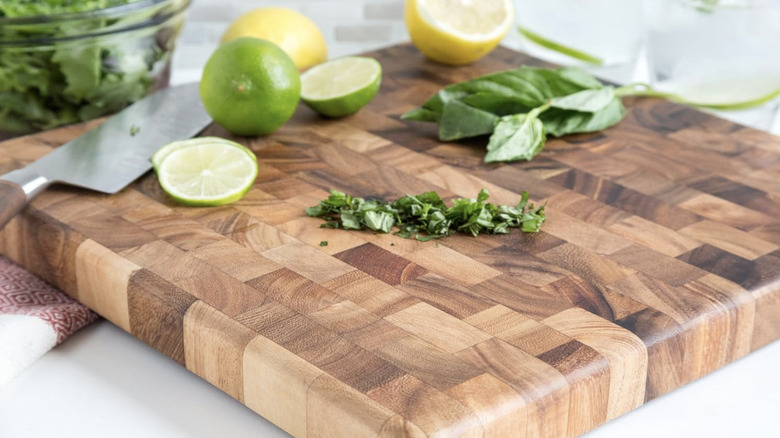 A square acacia wood cutting board being used to chop herbs and citrus