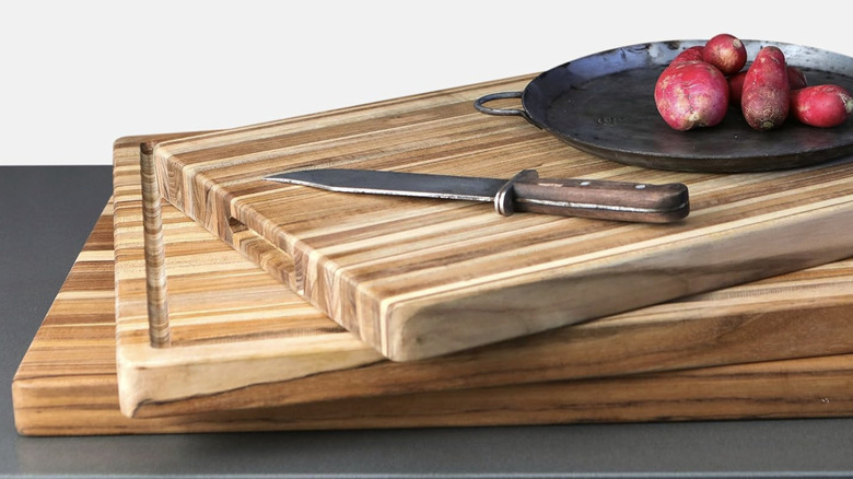 A knife and a plate of radishes sitting on three teak cutting boards