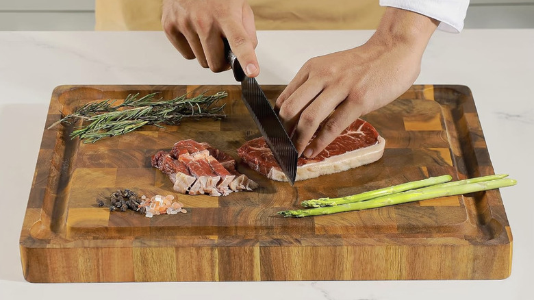 A person slicing meat on an acacia cutting board