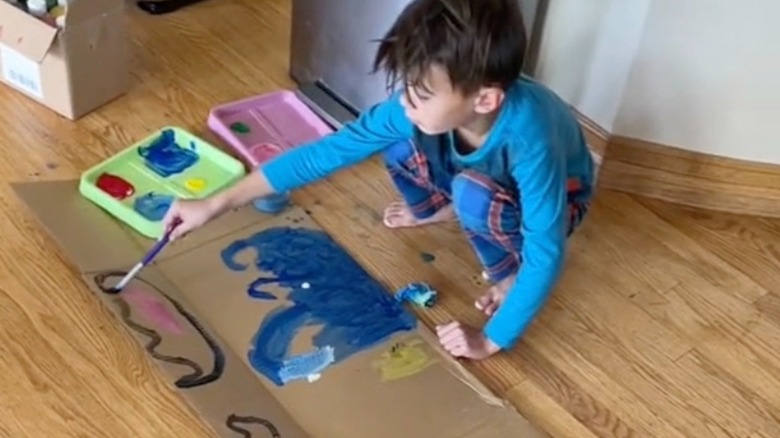Child painting on a cardboard box that has been opened up and laid flat on the ground.