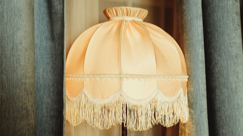 A neutral colored fringed lamp shade sitting next to curtains