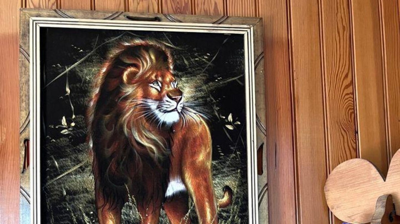 Velvet painting of a lion hanging on a wood paneled wall