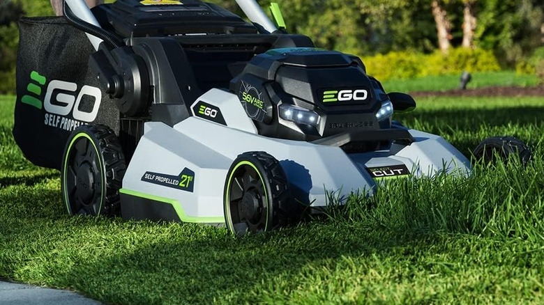 An electric lawn mower cutting thick grass