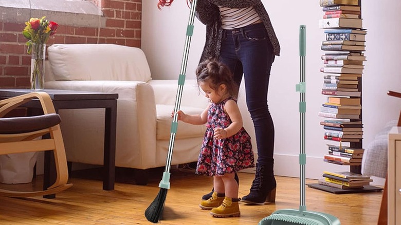 A little girl helping a woman sweep with a broom and dust pan