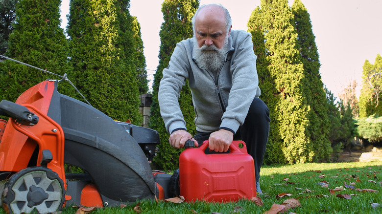 Gardener refilling lawn mower from red gas can.