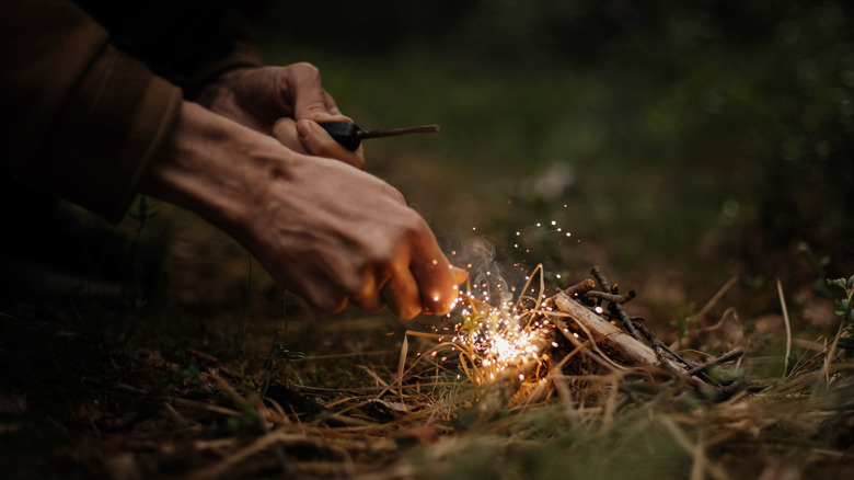 A person uses a ferro rod to create sparks in a pile of tinder gathered in a garden.