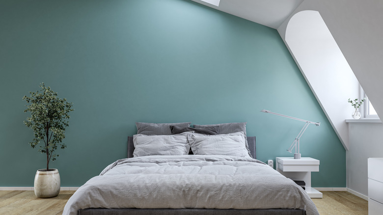 gray bed and bedding in front of a teal wall