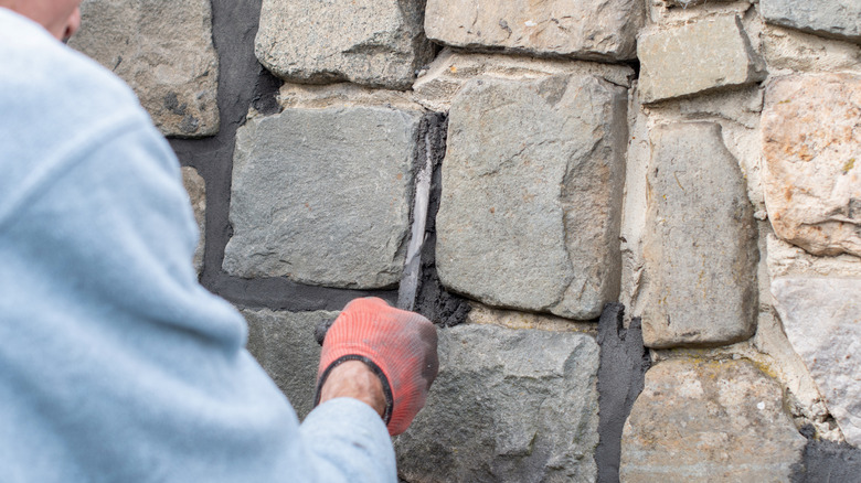 Hand applying mortar between blocks of a stone wall