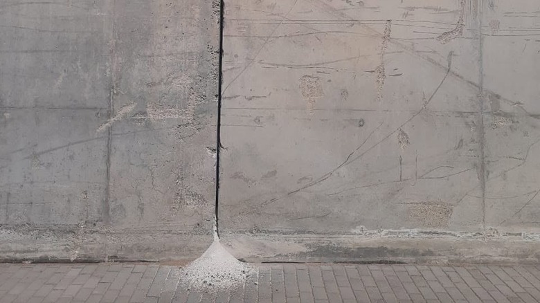 Two sections of cement wall separated by a wide gap in the seam, at the base of which is a pile of fine cement dust