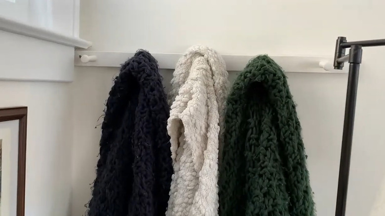 Three fuzzy blankets hanging from simple white hooks in the corner of the living room