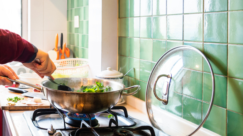 A person cooking in a pan on the stove in front of a green tile backsplash