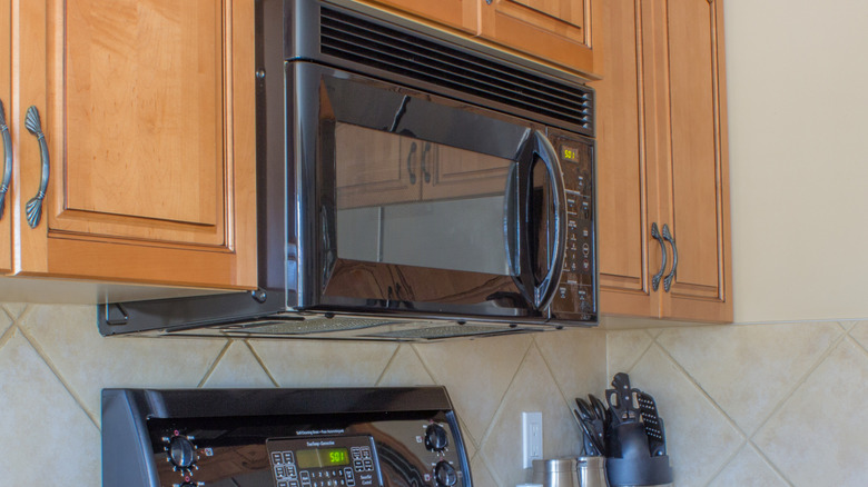 A black over-the-range microwave situated between wooden cabinets