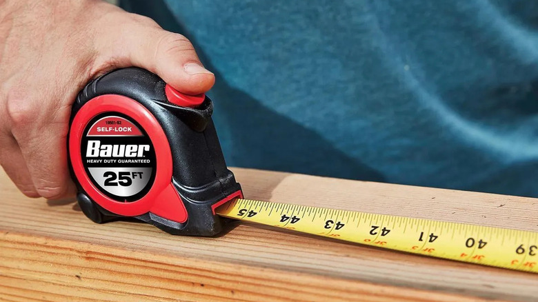 Person measuring a wood block with a Bauer tape measure