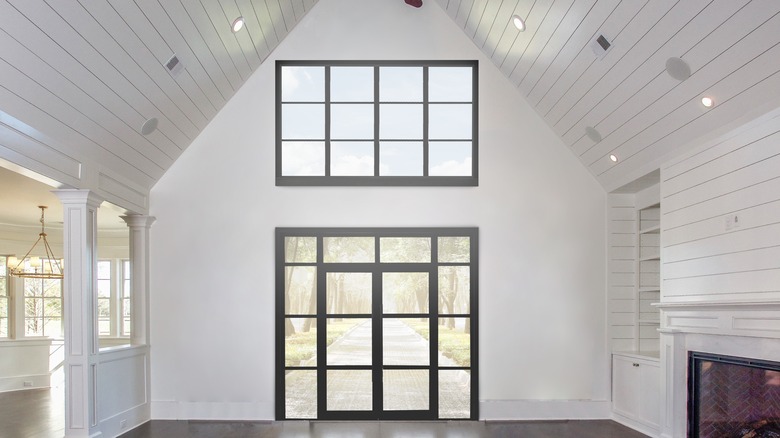 A modern farmhouse living room with a high vaulted ceiling and large black-trimmed windows.