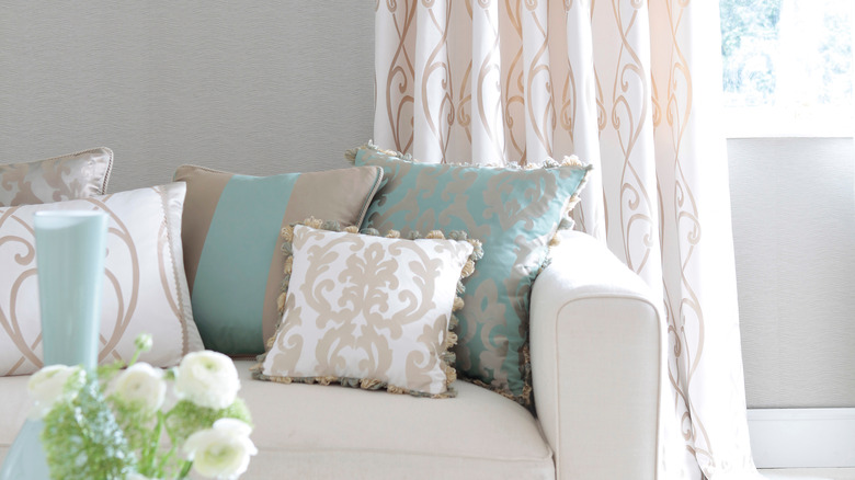 A couch with light patterned pillows next to a window with matching patterned drapes.