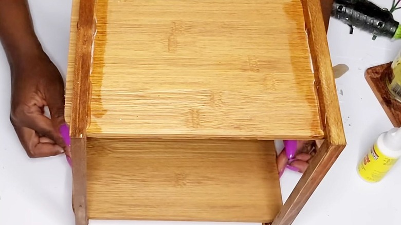 Hands place the bottom board onto a wooden countertop shelf.