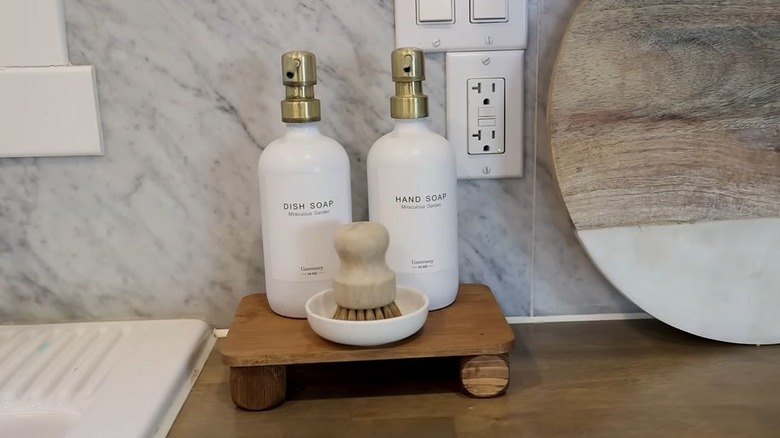 A wooden tray holds soap dispensers and a brush by a sink on the countertop.