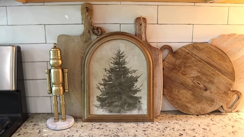 Wooden boards and a painting of a Christmas tree lean against a tile wall.