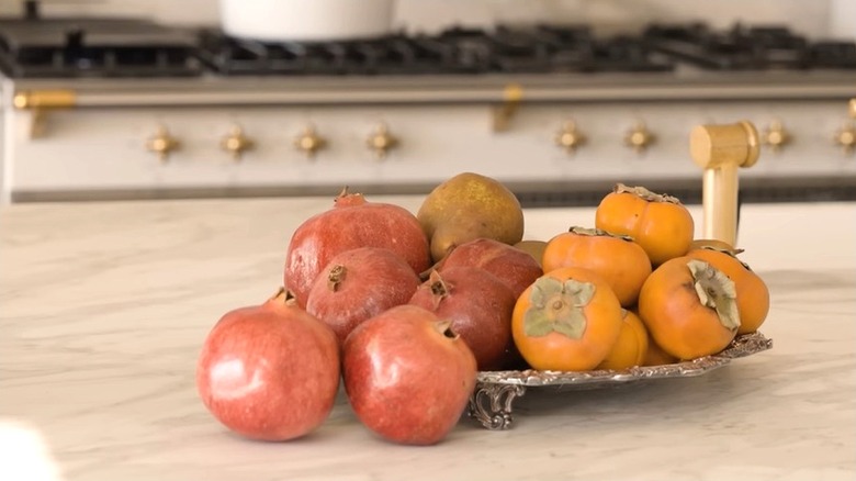 Persimmon and pomegranates on silver tray over marble kitchen island.