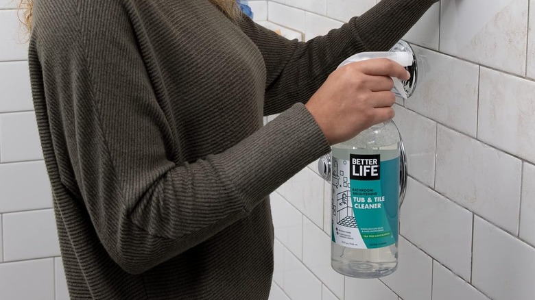 A person sprays Better Life Tub & Tile Cleaner on subway tiles in a grimy shower