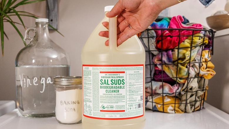 A person reaches for a gallon of Dr. Bronner's Siberian Fur & Spruce-scented Sal Suds Biodegradable Cleaner