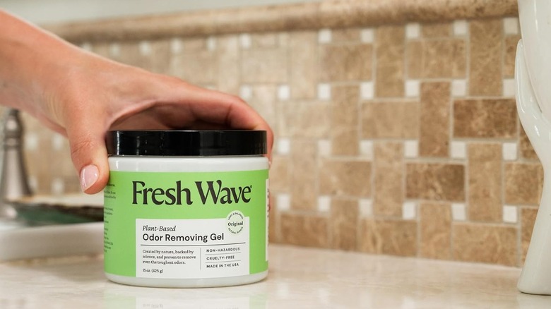 A person sets a container of Fresh Wave Plant-Based Odor Removing Gel on a bathroom counter
