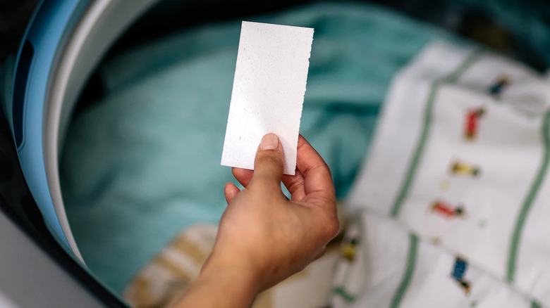 A person holds a Tru Earth Laundry Detergent Sheet above a washing machine full of clothes