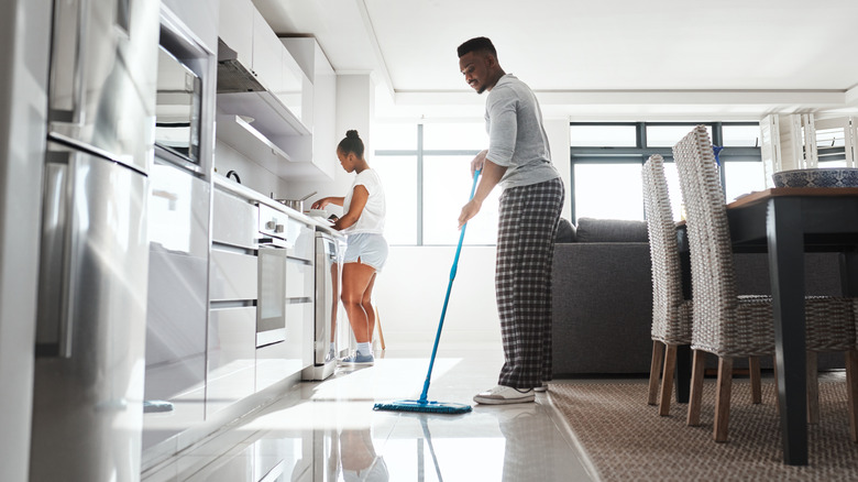 Young couple cleans the kitchen, man sweeping floor