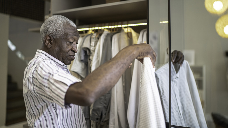 Older man hanging white button-up shirt in a closet.