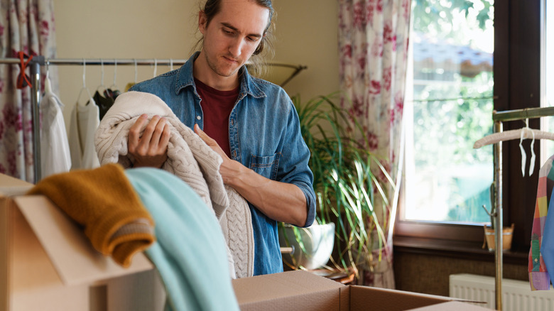 Man sorting through clothes to donate in cardboard boxes.