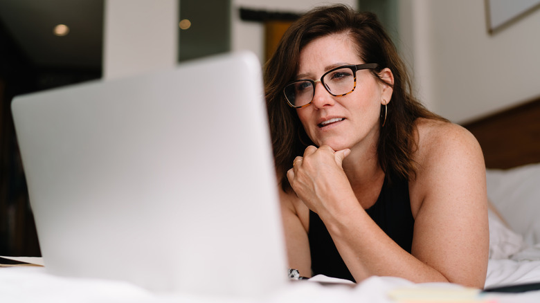 Woman looking at laptop computer while laying in bedroom.