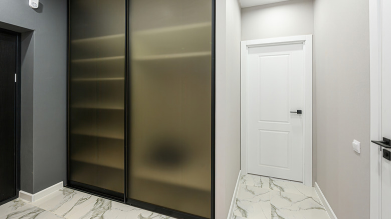 Corner closet with glass doors in a room with marble floors.