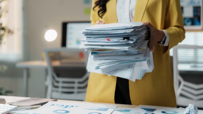 Woman in yellow suit holding a large stack of paper