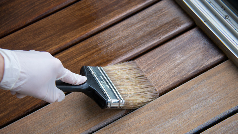 Gloved hand staining wood with a paint brush