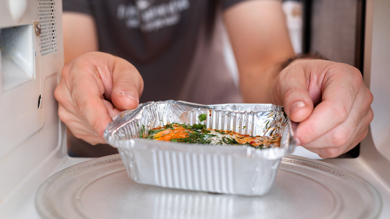 Hands placing a foil dish with food in it in the microwave.