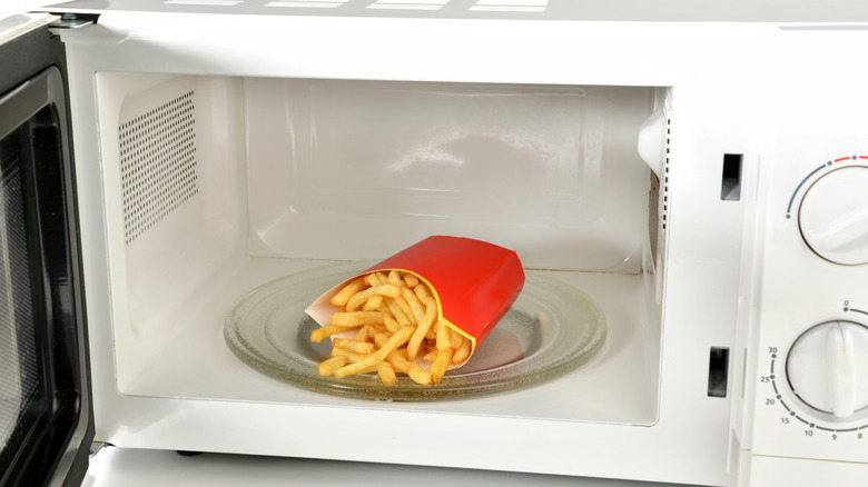 French fries in a cardboard coated container in a microwave.