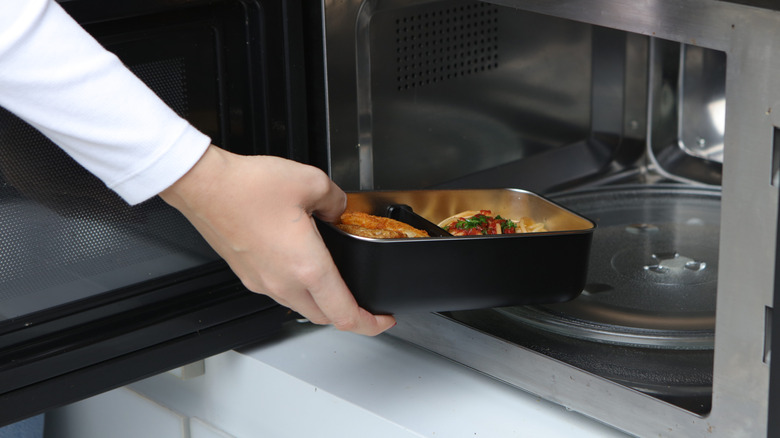 Hands inserting a metal container with food in it in the microwave.