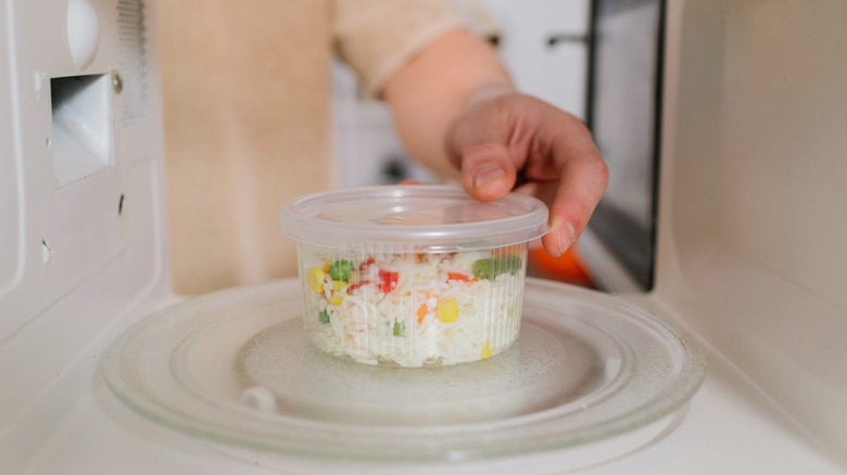 Hands placing a clear plastic dish into a microwave.