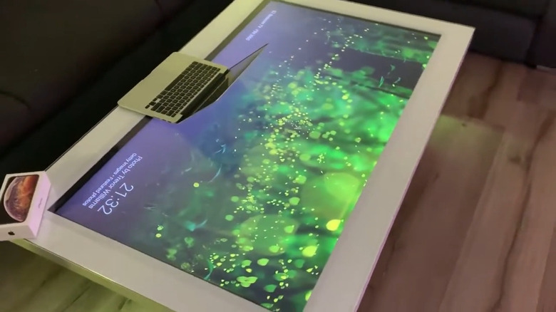 Flatscreen TV made into a gaming table, a laptop and Apple phone box on top