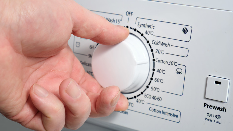 Hand turning the temperature dial on a washer