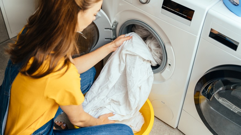 Woman loading white sheets into machine