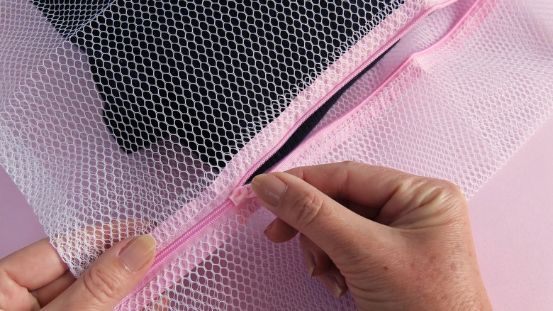 Hand zipping up a pink mesh laundry bag