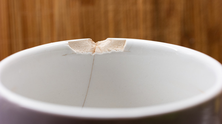 Closeup of a ceramic cup with a chipped edge against a wood background