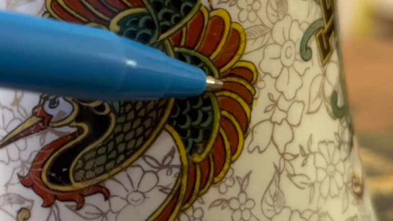 Blue ballpoint pen pointing to design on a richly-decorated cup with a bird motif