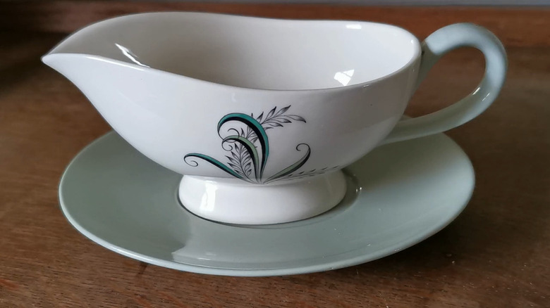 Closeup of a Spode gravy boat with a floral accent in green, black, and white shades on a wooden surface