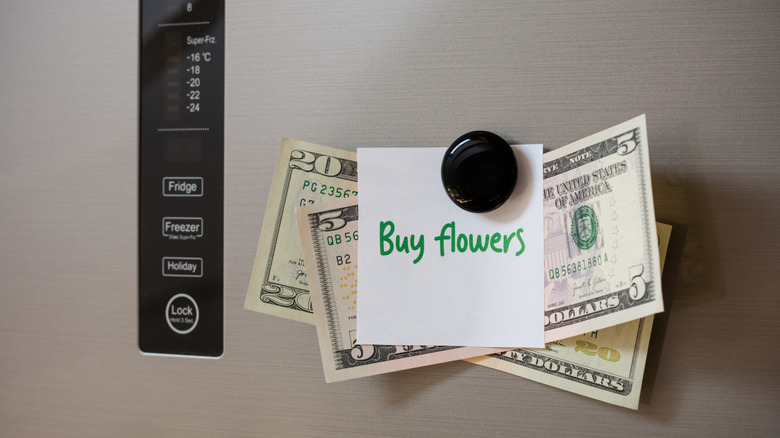 A black magnet on fridge holding money and a note